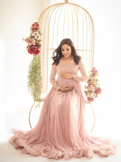 A serene portrait of the mom-to-be seated in our golden birdcage chair, surrounded by flowers. The soft pink gown adds to the romantic feel.