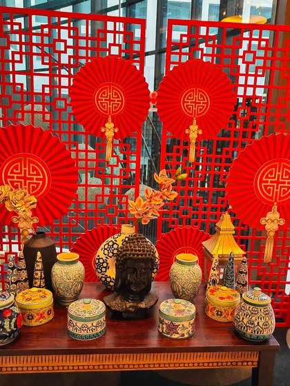 A beautifully styled console table for a Hakka Chinese Cuisine Food Festival. The setup includes a red lattice backdrop, paper fans, and a collection of ceramic jars and a Buddha head, creating an authentic and visually rich display.