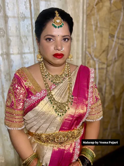 A powerful and regal bridal look. The deep red lipstick and defined eyes create a striking contrast with the cream and pink silk saree and antique jewelry.