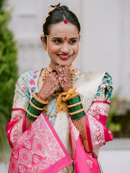 A joyful portrait of the bride, Kanchan, her hands clasped in happiness, showcasing her traditional 'mundavalya' and nose ring.