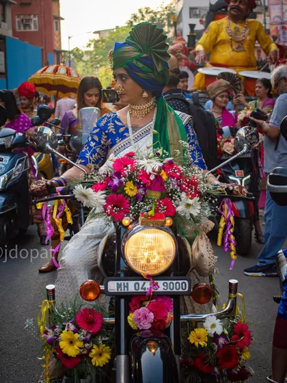 A woman in a traditional saree and ornate turban rides a motorcycle heavily decorated with flowers during the Gudi Padwa procession in Mumbai.