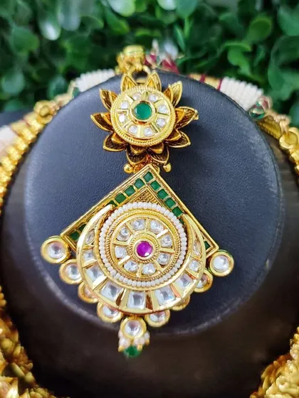 A close-up of the maang tikka from the grand bridal set seen in image 130. The intricate design and combination of stones are clearly visible.