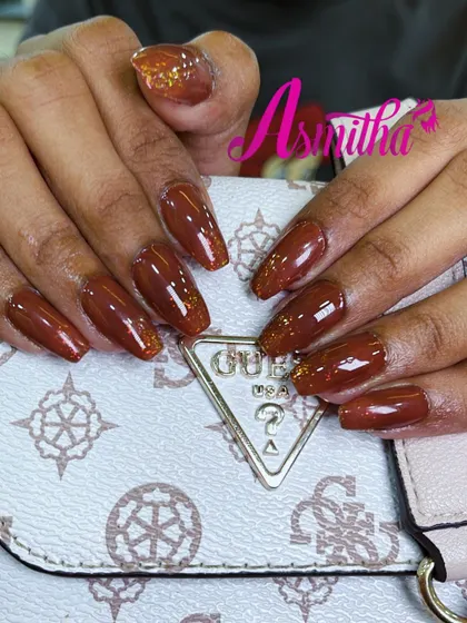 A happy client showing off her new coffin-shaped nail extensions. The design features a warm brown color with a subtle glitter fade on the tips.