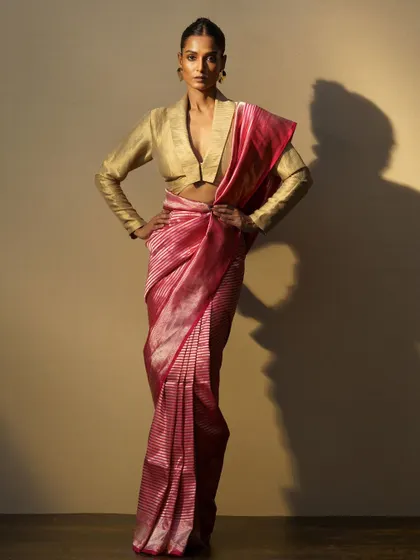 A striped pink silk saree paired with a structured gold blouse. This look is a beautiful example of modern power dressing with a traditional twist.