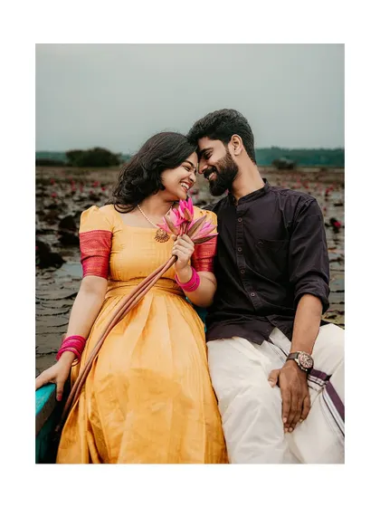 A romantic portrait of a couple touching foreheads in a boat, a single lotus flower connecting them.