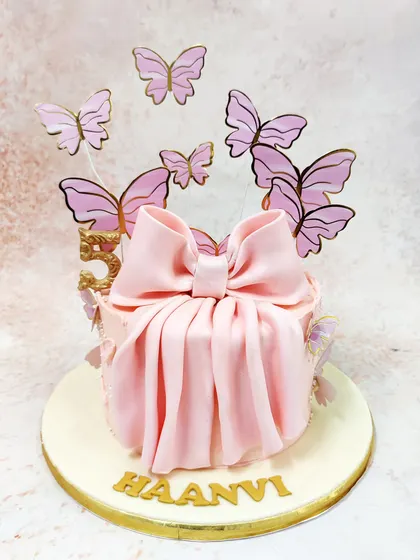 We present a gift of pure elegance with this pink bow cake. A large, beautifully draped fondant bow is the centerpiece, surrounded by a flight of ethereal pink and gold butterflies, making the cake itself look like a precious, unopened present.