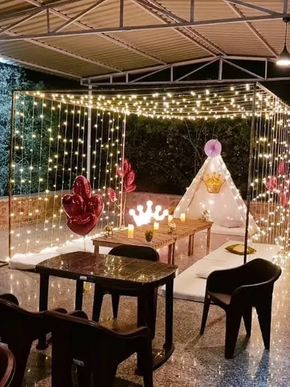 A cozy and royal-themed terrace decoration. This setup features a canopy of fairy lights, a small tent, and low seating, creating a magical and intimate space for a small gathering.