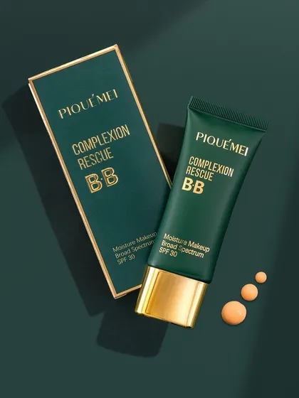 A luxurious shot of PiqueMei's Complexion Rescue BB cream. The combination of the royal green packaging with gold accents against a matching dark green background creates a feeling of premium quality and elegance.