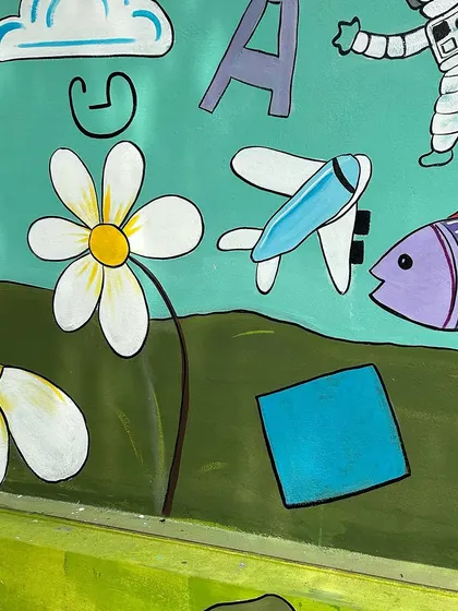 More details from the school wall, including an airplane, a fish, and letters of the alphabet floating among the clouds.