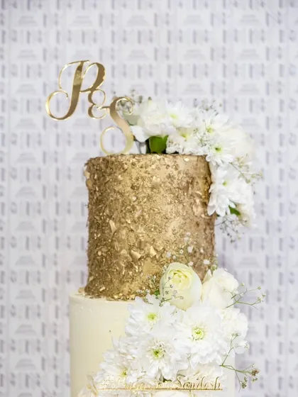 A close-up of our elegant gold and white wedding cake. The textured gold finish of the top tier contrasts beautifully with the fresh white flowers and the couple's monogram topper.