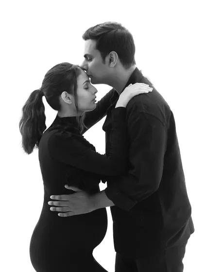 A timeless black and white portrait of the couple. His gentle kiss on her forehead and their simple, coordinated outfits create a classic and loving image.