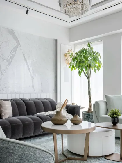 This living room embodies elegance with its calming blue palette and light, airy fabrics. The space is anchored by a plush charcoal sofa and features intricate wall moulding combined with opulent marble.