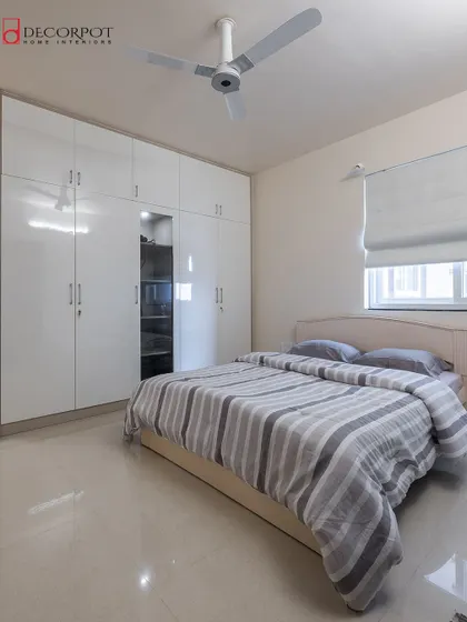 This bedroom design focuses on simplicity and brightness, with a glossy white floor-to-ceiling wardrobe. The clean lines and reflective surface help to create a spacious and uncluttered feel.