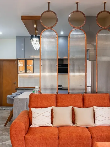 A full view of the open living and kitchen area, separated by a stylish mirrored partition. The orange sofa provides a bold contrast to the neutral walls and grey kitchen cabinets.