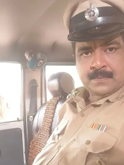 In the driver's seat, in character as a police officer for 'Room No. 111'.