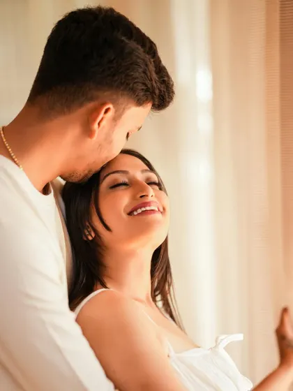 An intimate and cozy indoor shot of a couple sharing a tender moment by a window, bathed in soft natural light.