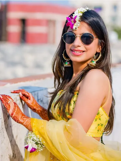 A sun-kissed portrait of the bride at her outdoor Haldi ceremony. Her floral maang tikka and bright smile perfectly capture the cheerful and natural mood of the event.