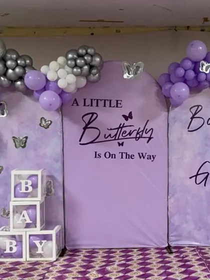 A butterfly-themed "Boy or Girl?" baby shower backdrop. The purple panel is framed by a purple, white, and silver balloon arch.