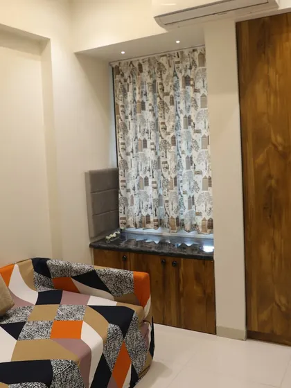 A cozy guest bedroom with a sofa-cum-bed, a wooden wardrobe, and a window seating area with storage below.
