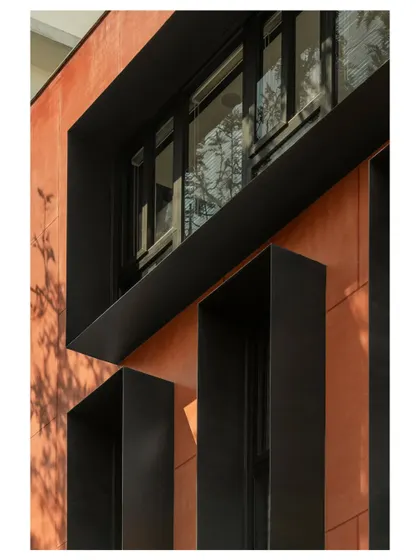 A close-up of the facade's architectural details. The black metal fins and window frames provide a sharp, graphic contrast to the warm red walls, highlighting the building's structural grid.