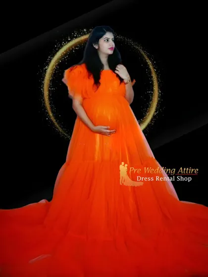 Another look at the vibrant orange ruffled gown in a studio setting. The simple background allows the dress's bold color and full skirt to be the complete focus of the maternity photograph.