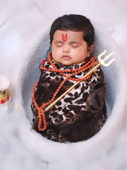 A wider view of the 'Little Shiva' setup, with the baby surrounded by a fluffy white 'cloud' base and miniature damaru drums.
