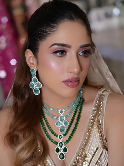 This portrait showcases the complete look, with the model adorned in stunning emerald jewelry that contrasts beautifully with the soft makeup.