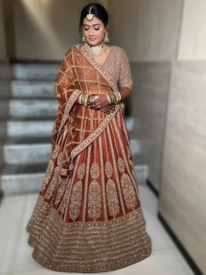 A full-length shot of the bride in her stunning rust-colored lehenga. The makeup is designed to complement the unique color palette, with warm tones and a radiant finish.