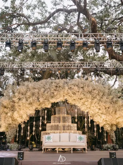 A closer view of the sangeet stage, featuring a massive arch of white baby's breath, hanging crystal details, and elegant seating for the couple.