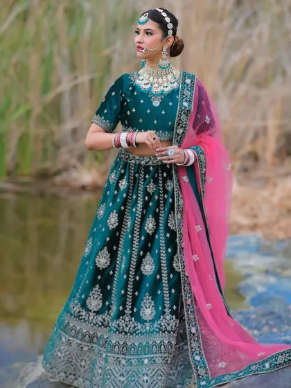 A stunning teal velvet lehenga with silver embroidery and a contrasting pink dupatta, perfect for a modern bride.