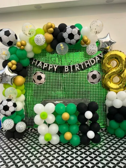 Another angle of a football theme party setup, this one on a rooftop. The green sequin backdrop mimics a football field, framed by a balloon arch with football and star-shaped foil balloons.