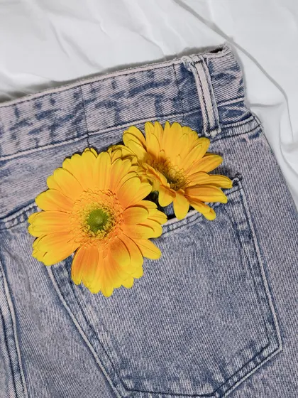 A lifestyle flat-lay of the H&M jeans with flowers in the pocket. This styling adds a touch of personality and softness, making the product more relatable for social media.