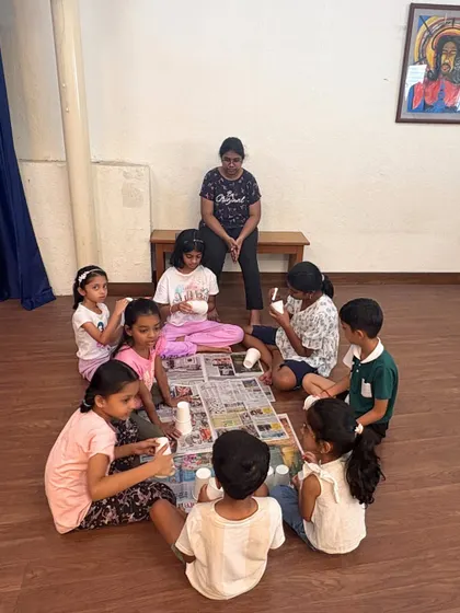 An instructor sits with a group of young girls as they work on their paper cup crafts. We ensure small group sizes so every child gets the attention and guidance they need to succeed.