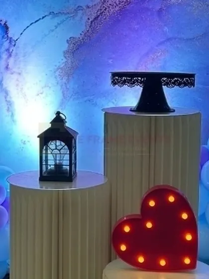 A close-up of props for a modern baby shower, including a light-up heart, a decorative lantern, and a cake stand against a blue marbled backdrop.