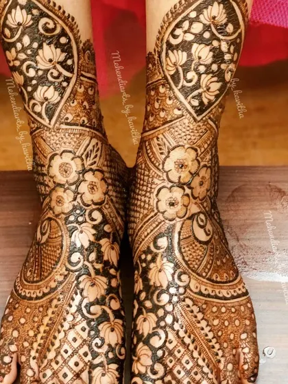 This full-coverage bridal feet mehendi is rich with detail. It features floral and lotus motifs on the ankles and a dense pattern of flowers and checks covering the feet.