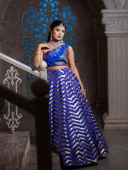 The model posing on a staircase in the blue and gold lehenga, showcasing its elegant and structured design.