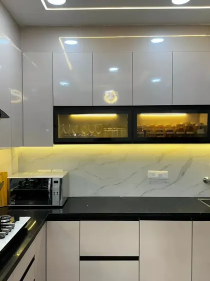A sleek and modern modular kitchen with glossy white cabinets, a black countertop, and under-cabinet lighting that provides both task lighting and ambiance.