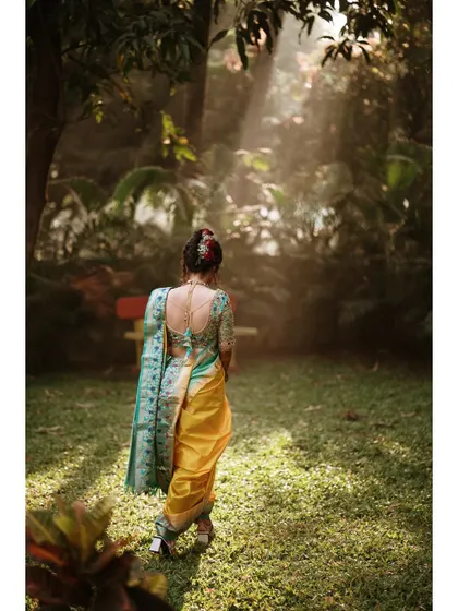A beautiful back-shot of the bride walking into a sunlit garden. This portrait highlights the intricate design of her blouse and her graceful posture.