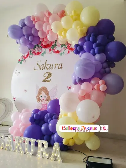 A beautiful Sakura-themed second birthday with a floral and butterfly backdrop, a dense balloon arch in shades of purple, pink, and yellow, and marquee letters.