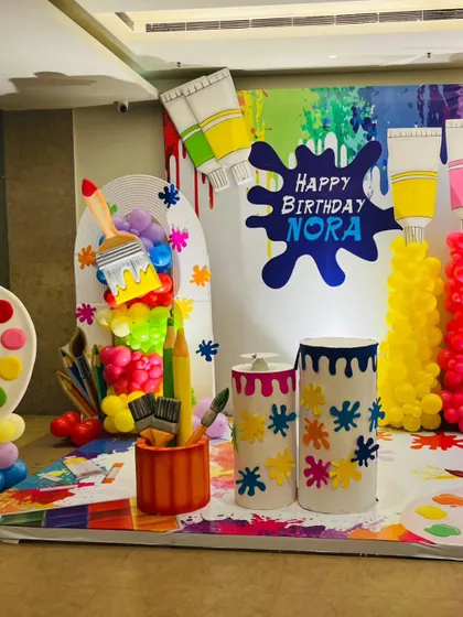 The main photo booth for an art-themed birthday party. The backdrop features giant paint tubes, brushes, and a colorful paint splash with the birthday girl's name.