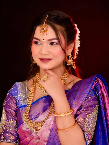 A close-up portrait highlighting the flawless base and eye makeup. The lighting accentuates the highlighter and the rich colors of her attire.