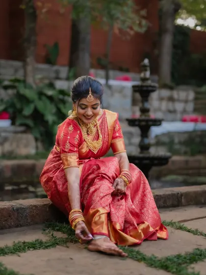 A portrait of the bride in her stunning red saree, framed by the rustic charm of her wedding venue. We focus on creating images that are both beautiful and full of character.