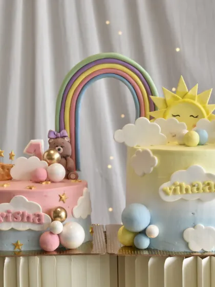 A pair of adorable matching cakes for a joint birthday party. One features a teddy bear and moon theme, while the other has a sun and clouds theme.