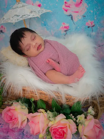 A beautifully styled shot of a newborn girl in a basket with a tiny parasol. The floral backdrop and soft textures create a dreamy, picturesque scene.