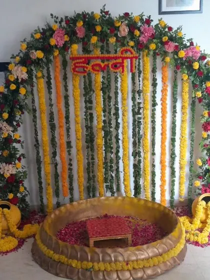 A classic floral arch backdrop for a Haldi ceremony. The arch is made of colorful flowers and marigolds, with hanging garlands creating a curtain-like effect behind the main ritual area.