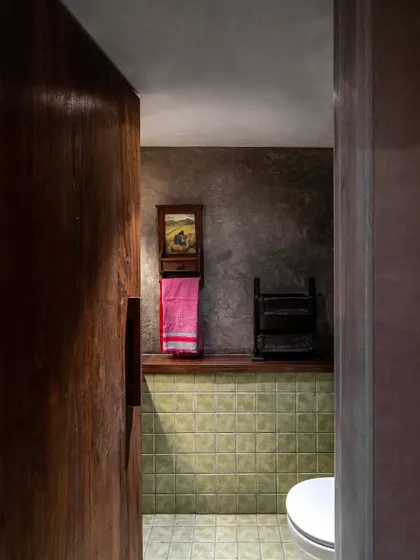 This washroom continues the home's raw and natural design language. Earthy green tiles and an exposed concrete finish create a contemporary yet familiar feel, with repurposed details adding a sense of history.