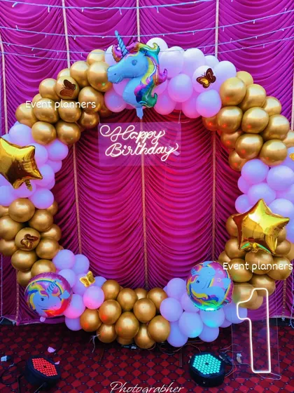 This is a closer look at the unicorn-themed birthday backdrop. The combination of chrome gold and pastel white balloons, along with the glowing neon sign and light-up number '1', creates a rich and festive look for a first birthday.