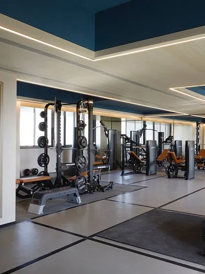 The gym follows a grey, white, and black color palette, with blue painted ceiling coves and linear lighting to create a dynamic and motivating workout environment.