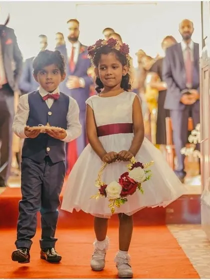 Walking down the aisle with grace. This custom flower girl dress in pure white features a simple, elegant silhouette with a contrasting red sash, perfectly matching the wedding's color scheme.
