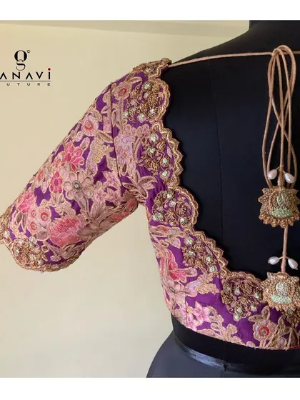 The back of a floral print blouse with a scalloped, embroidered edge. The intricate beadwork and threadwork follow the contours of the design, finished with beautiful custom tassels.